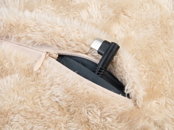 Connecteur USB noir et argenté dépasse d'une fermeture à glissière beige entrouverte sur un tissu en fausse fourrure crème