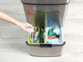 Personne effectuant le tri des déchets grâce aux divers compartiments de la poubelle Infactory en jetant les cartons dans un conteneur et les déchets alimentaires dans un autre