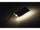Pince en métal avec LED allumée dans l'obscurité pour éclairage de surfaces en verre, avec câble d'alimentation noir branché et 3 LED blanc chaud sur la pince/clip de fixation, reflétées par la paroi éclairée