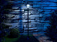 Lampadaire à LED blanc lumière du jour allumé dans l'obscurité d'un jardin devant un mur en pierre