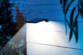 Mise en situation du spot solaire fixé à un mur en briques blanches dans un jardin en extérieur éclairant un chemin d'une lumière blanche