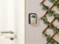 Boîte à clefs sécurisée à code manuel fixée à un mur taupe à côté d'une porte et d'une plante grimpante