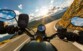 Moto roulant sur une route de montagne avec à son bord une personne avec des gants de moto la pilotant et sur son guidon étant installée l'enceinte nomade JBL