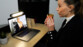 Femme maquillée et habillée chic tenant dans ses mains un verre devant la webcam d'un ordinateur portable sur lequel est fixé la lampe LED YouniLight