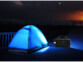 Utilisation de la lumière LED de la batterie d'appoint dans l'obscurité devant une tente de camping bleue montée
