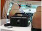 Générateur solaire HSG-980 branchée à l'adaptateur secteur fourni posée sur une table vernis blanche à l'arrière d'un véhicule conduit par un homme à la cinquantaine