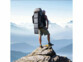 Homme randonneur en short et t-shirt debout sur un rocher contemplant la vue sur les montagnes et les nuages les surplombant avec sur le dos un grand sac à dos dont dépasse le panneau solaire pliable 28 W Revolt