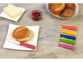 Couteau rouge posé sur une assiette carrée blanche à côté d'une boule de pain coupée en deux à côté de 5 couteaux aux coloris différents (orange, jaune, vert, rose, bleu foncé)