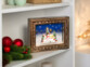 Cadre décoratif de Noël "Bonhommes de neige" posé sur une étagère blanche à côté d'une décoration de Noël avec branches de sapin et boules rouge brillant