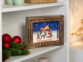 Cadre décoratif de Noël "Village de Noël" posé sur une étagère blanche à côté d'une décoration de Noël avec branches de sapin et boules rouge brillant
