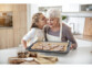 Grand-mère et sa petite-fille l'embrassant sur la joue dans une cuisine aux tons beige et blanc faisant des petits gâteaux de Noël posés sur la plaque de cuisson extensible avec ingrédients style cannelle posés sur le plan de travail 