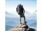 Homme debout sur la pointe d'un rocher en haute montagne observant la vue au-dessus les nuages à travers la montagne avec sur son dos un sac de randonnée auquel le panneau solaire pliable fourni en accessoire est attaché et déplié