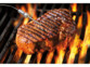 Steak en cours de cuisson sur un grille de barbecue sous laquelle se trouvent des flammes avec sonde filaire de mesure de la température plantée dedans