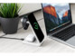 Station de recharge 3 en 1 branchée sur secteur par câble USB alimentation une Apple Watch, un iPhone et des EarPods sans fil à côté d'une plante en pot et d'un MacBook allumé